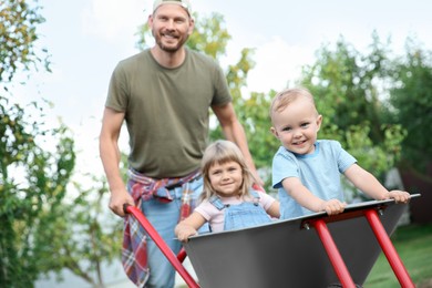 Photo of Father pushing wheelbarrow with his kids outdoors, selective focus