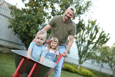 Father pushing wheelbarrow with his kids outdoors, space for text