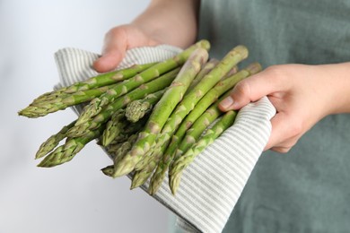 Photo of Woman with fresh asparagus stems on light grey background, closeup