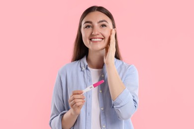 Happy woman holding pregnancy test on pink background