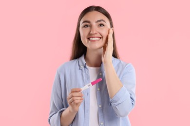 Photo of Happy woman holding pregnancy test on pink background