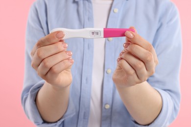 Woman holding pregnancy test on pink background, closeup