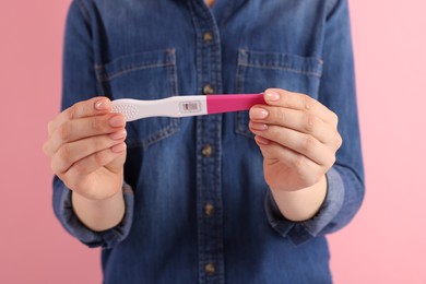 Photo of Woman holding pregnancy test on pink background, closeup