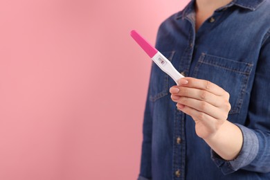 Woman holding pregnancy test on pink background, closeup. Space for text