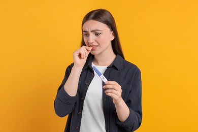 Photo of Sad woman holding pregnancy test on orange background