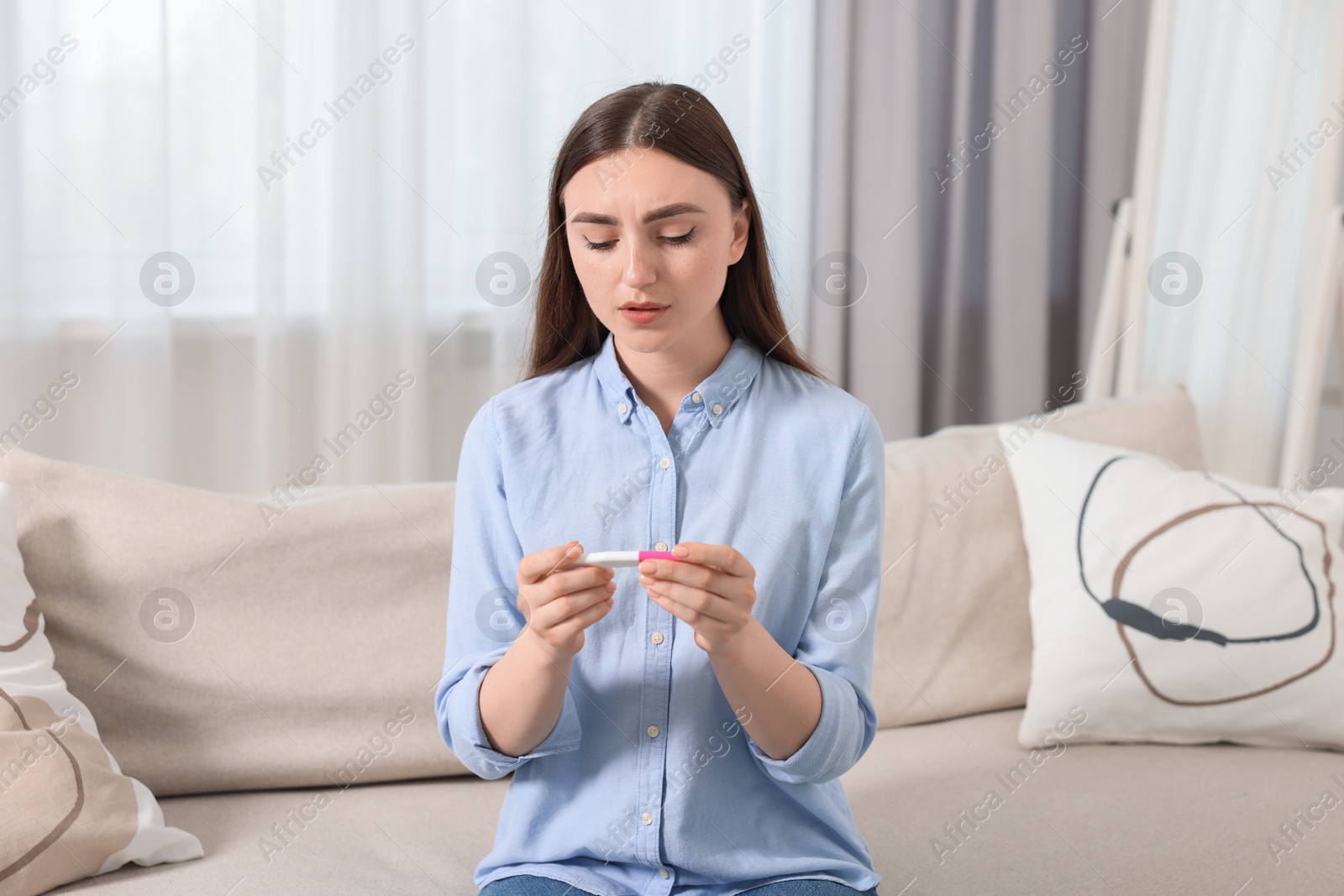 Photo of Sad woman holding pregnancy test on sofa indoors