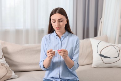 Sad woman holding pregnancy test on sofa indoors