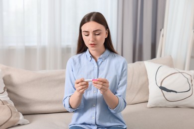 Photo of Sad woman holding pregnancy test on sofa indoors