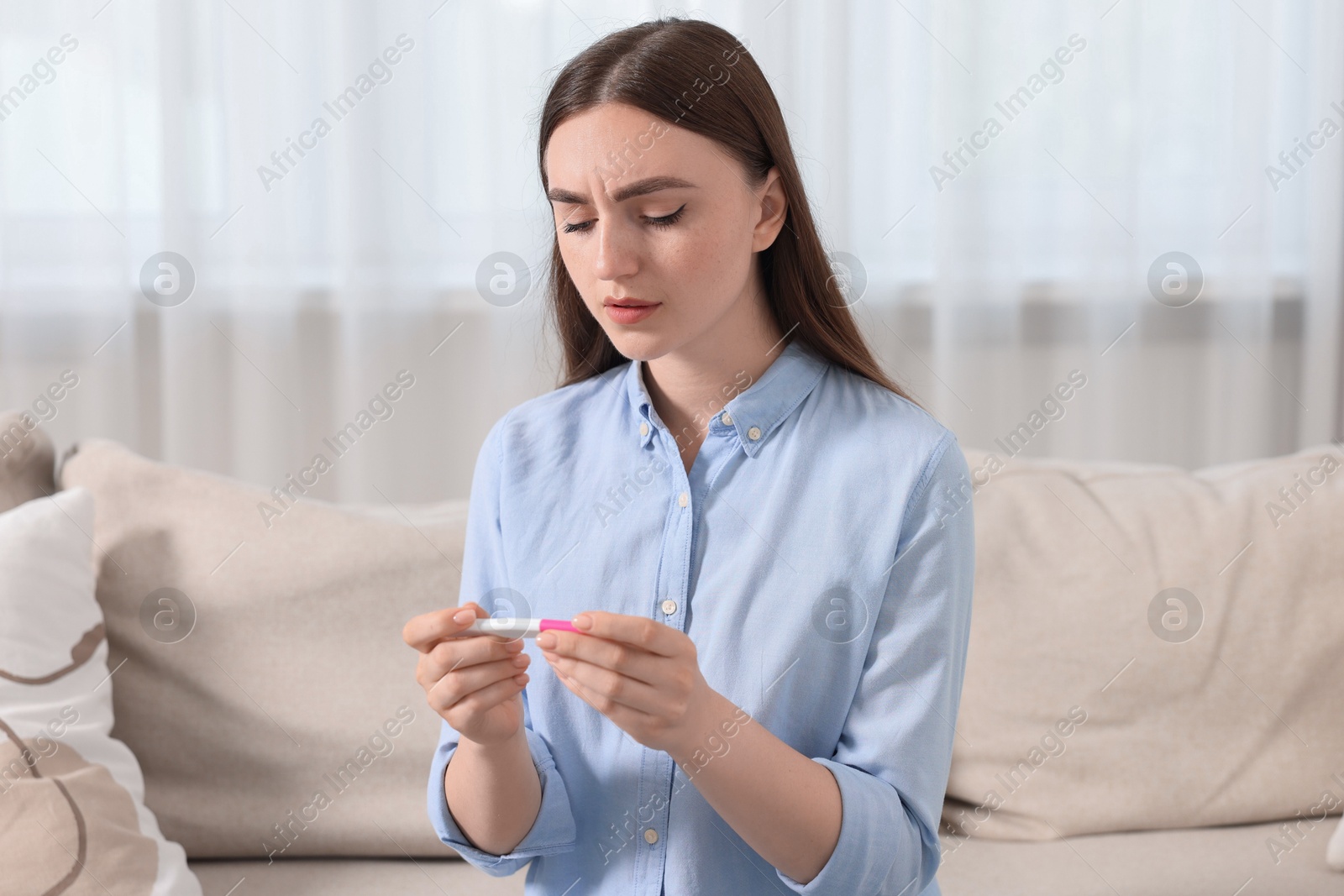 Photo of Sad woman holding pregnancy test on sofa indoors