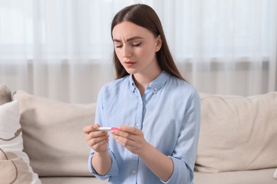 Sad woman holding pregnancy test on sofa indoors