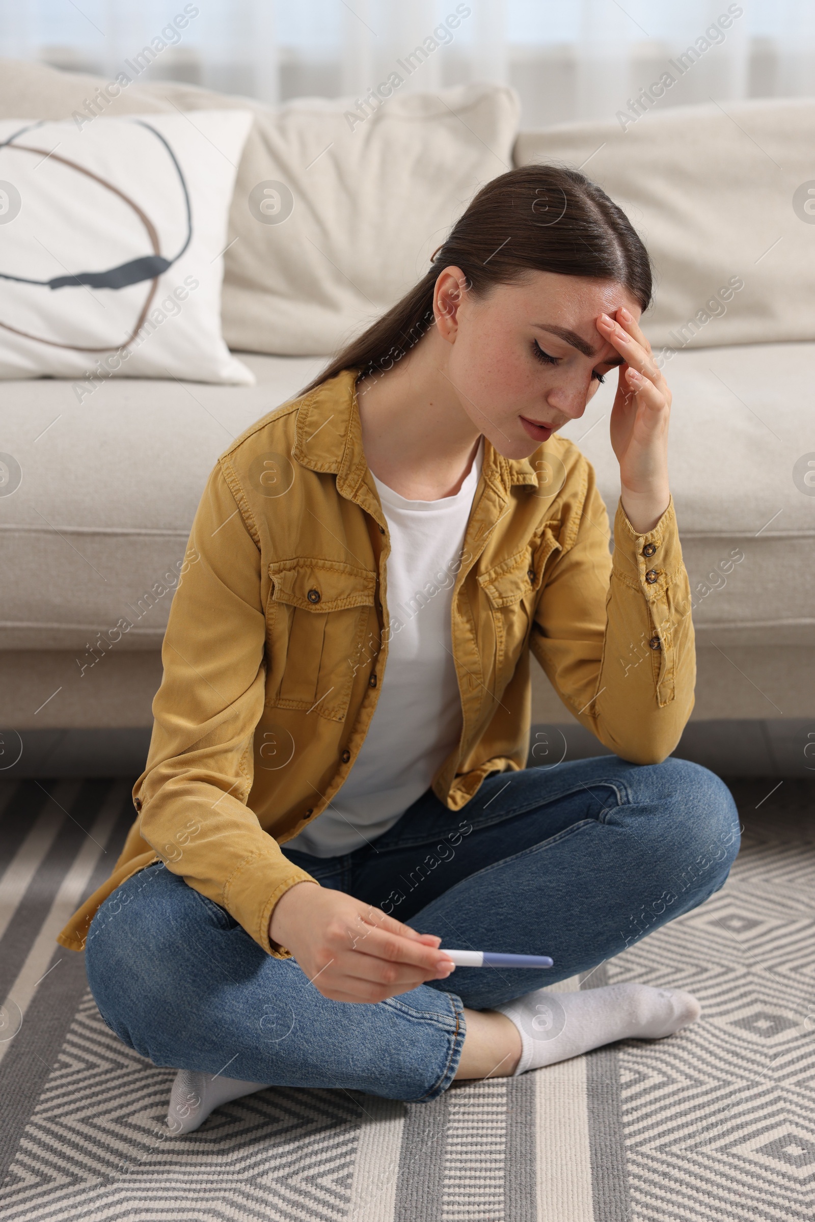 Photo of Sad woman holding pregnancy test on floor indoors