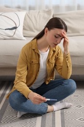 Photo of Sad woman holding pregnancy test on floor indoors