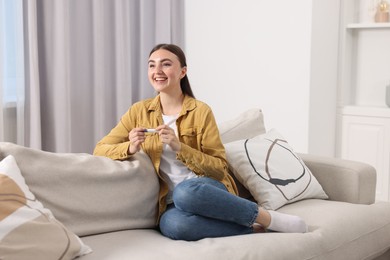 Photo of Happy woman holding pregnancy test on sofa indoors