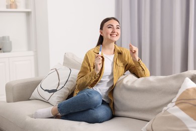 Photo of Happy woman holding pregnancy test on sofa indoors