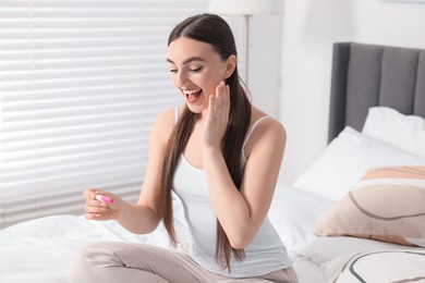 Happy woman holding pregnancy test on bed in room