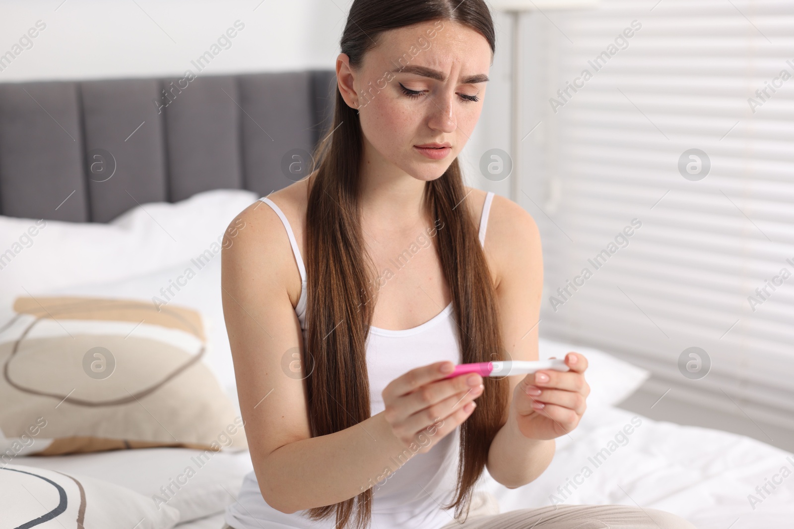 Photo of Sad woman holding pregnancy test on bed in room