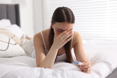 Sad woman holding pregnancy test on bed in room