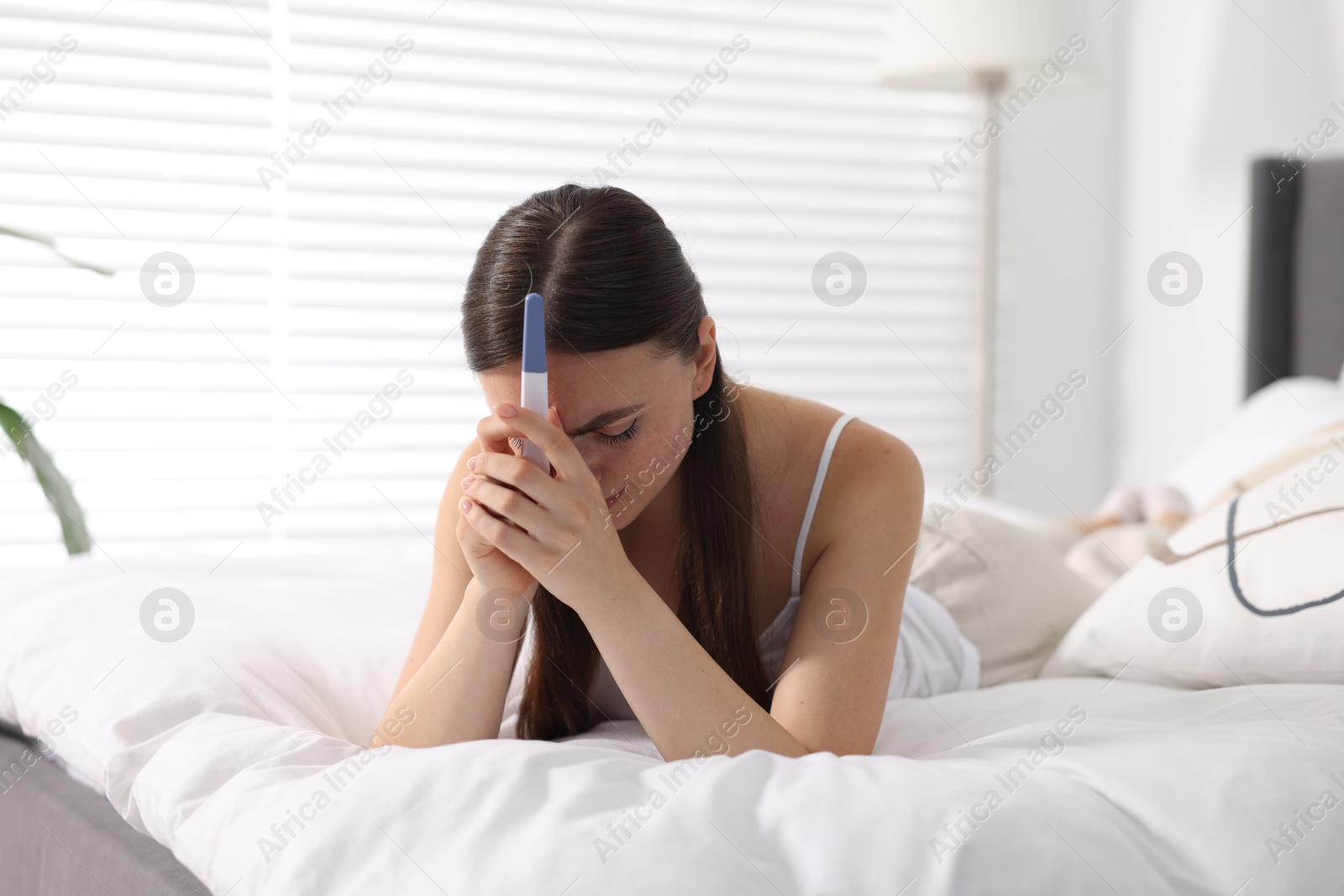 Photo of Sad woman holding pregnancy test on bed in room