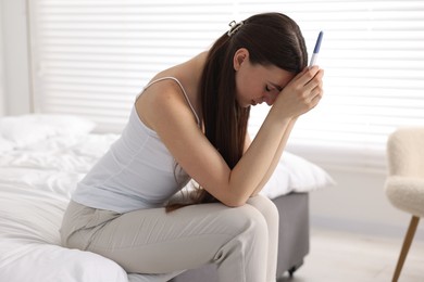 Photo of Sad woman holding pregnancy test on bed in room