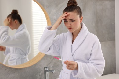 Sad woman holding pregnancy test in bathroom