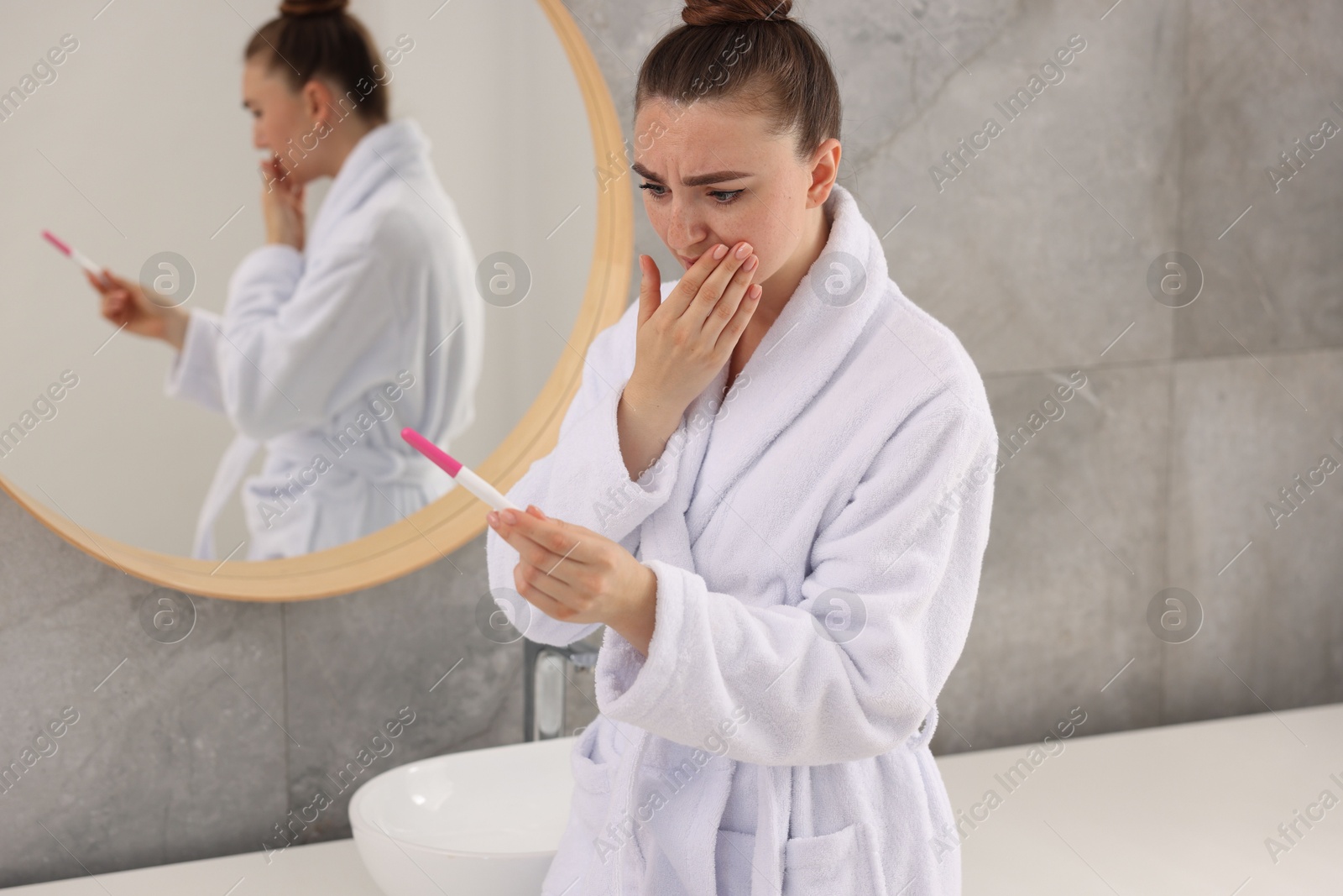 Photo of Sad woman holding pregnancy test in bathroom