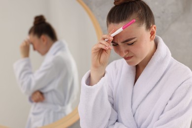 Sad woman holding pregnancy test in bathroom