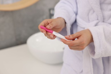 Woman holding pregnancy test in bathroom, closeup. Space for text