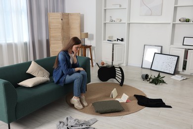 Photo of Desperate woman sitting on sofa in messy living room after robbery