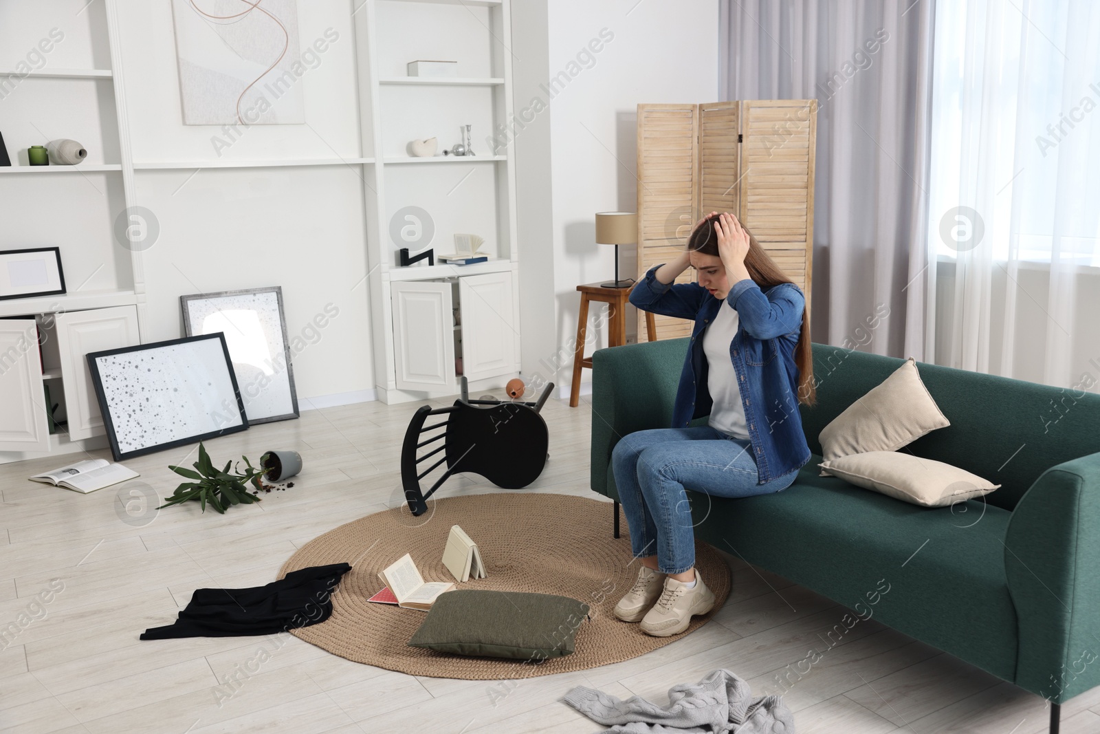 Photo of Desperate woman sitting on sofa in messy living room after robbery