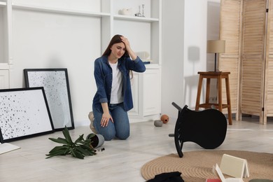 Photo of Desperate woman sitting on floor in messy living room after robbery