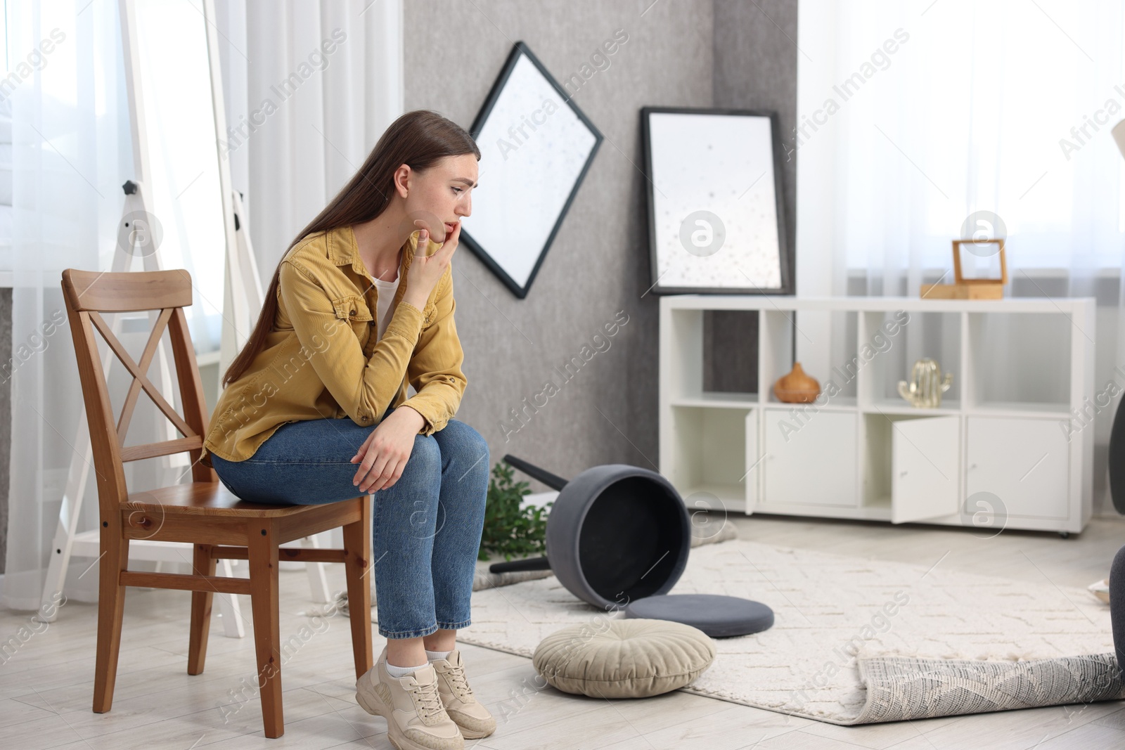 Photo of Desperate woman sitting on chair in messy living room after robbery