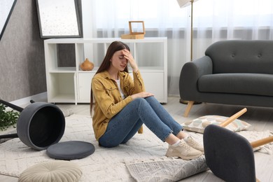 Photo of Desperate woman sitting on floor in messy living room after robbery