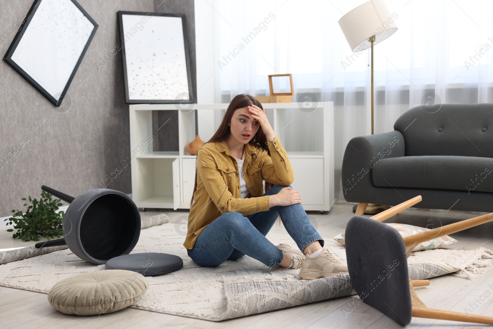 Photo of Desperate woman sitting on floor in messy living room after robbery