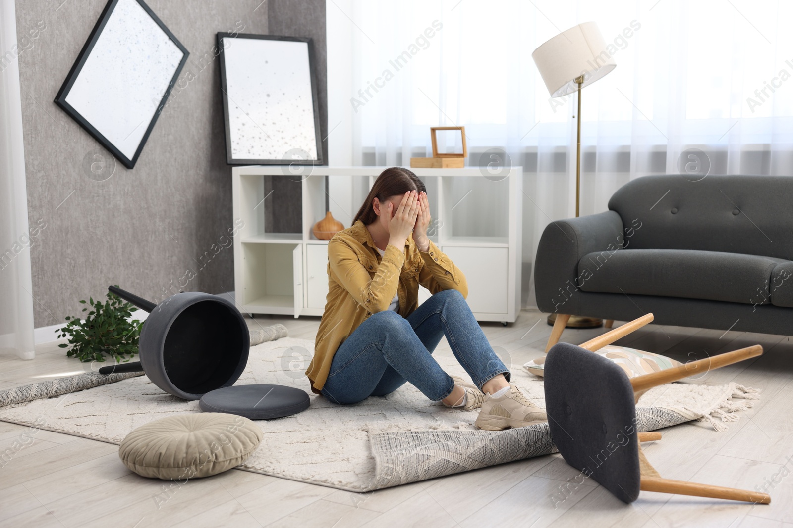 Photo of Desperate woman sitting on floor in messy living room after robbery