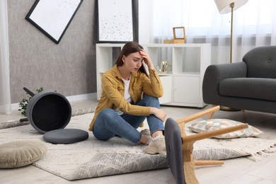 Desperate woman sitting on floor in messy living room after robbery