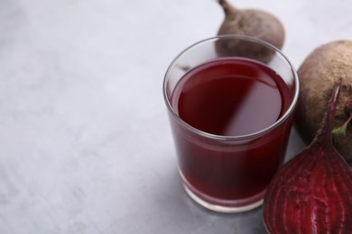 Photo of Fresh beet juice in glass and ripe vegetables on gray table, closeup. Space for text