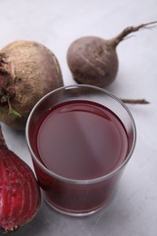 Photo of Fresh beet juice in glass and ripe vegetables on gray table, closeup