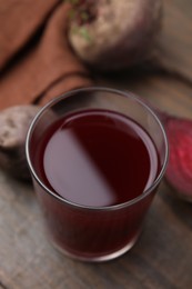 Photo of Fresh beet juice in glass and ripe vegetables on wooden table, closeup