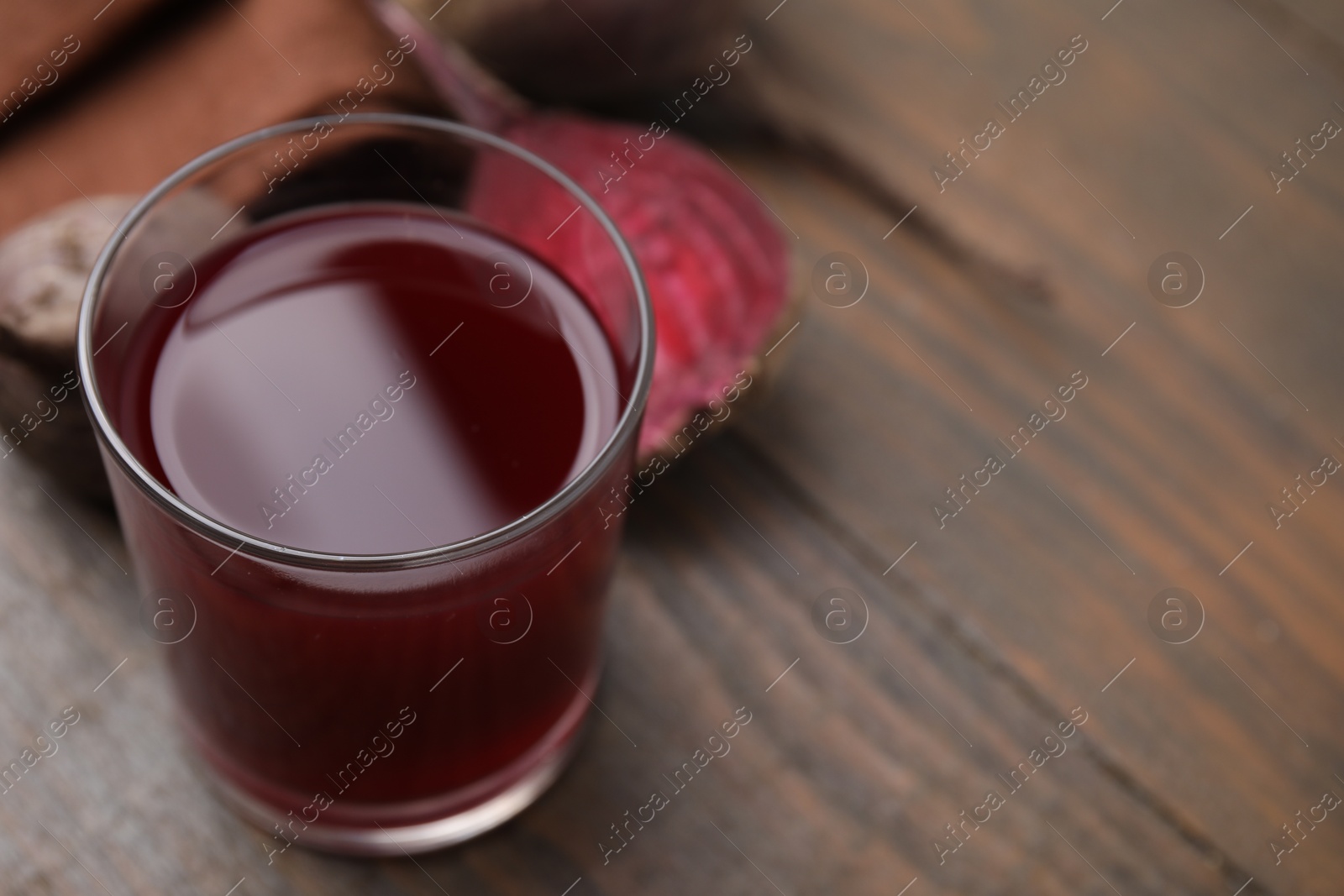 Photo of Fresh beet juice in glass on wooden table, closeup. Space for text