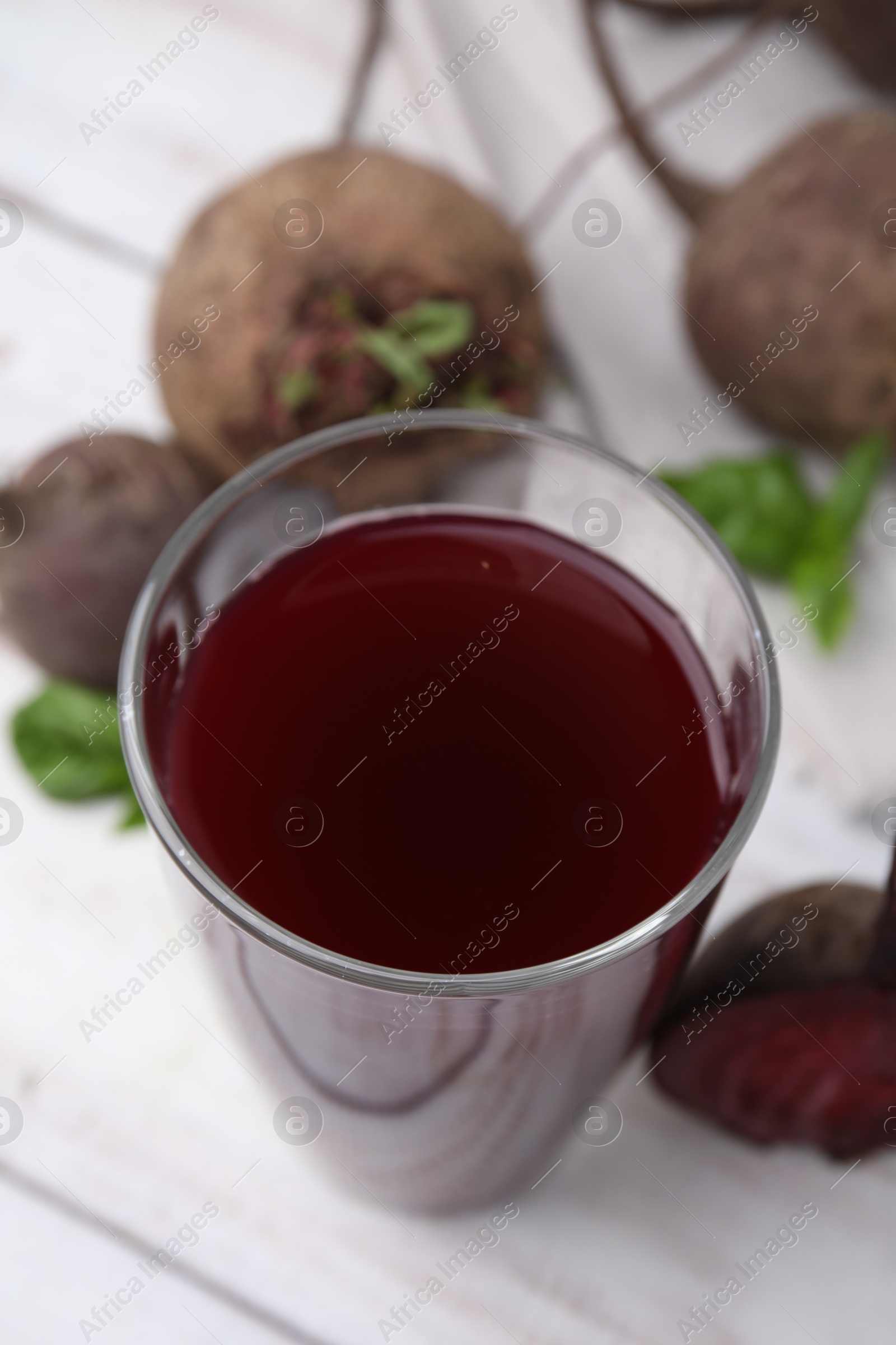 Photo of Fresh beet juice in glass and ripe vegetables on light wooden table, closeup