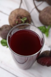 Photo of Fresh beet juice in glass and ripe vegetables on light wooden table, closeup