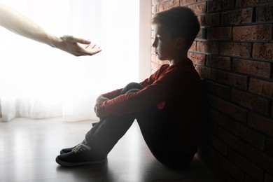 Image of Sad little child looking at outstretched man's hand in room. Trust, support, help