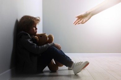 Woman offering hand to sad child indoors. Trust, support, help