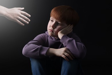 Image of Sad little child looking at outstretched man's hand in darkness. Trust, support, help