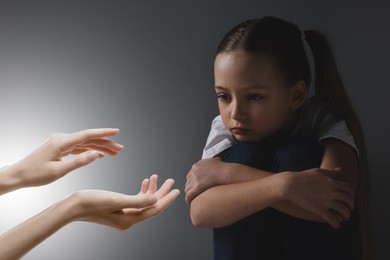 Sad little child looking at outstretched woman's hands in darkness. Trust, support, help