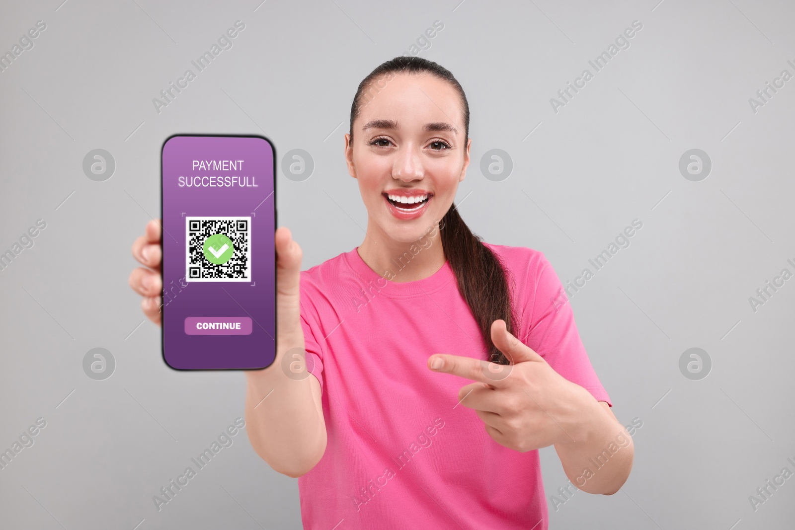 Image of Happy woman pointing at mobile phone with online payment application screen on grey background