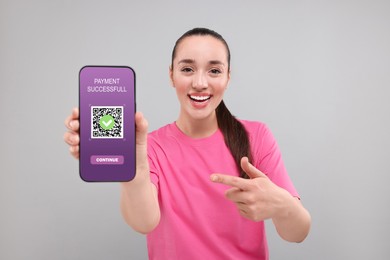 Happy woman pointing at mobile phone with online payment application screen on grey background