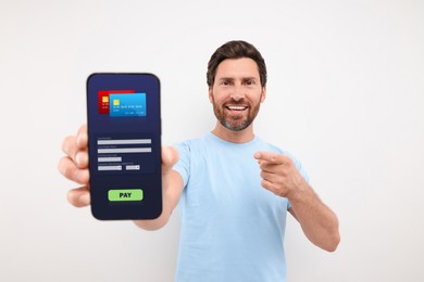 Happy man pointing at mobile phone with online payment application screen on light grey background