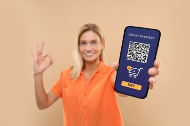 Happy woman showing Ok gesture and mobile phone with online payment application screen on beige background