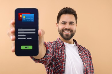 Happy man showing mobile phone with online payment application screen on beige background